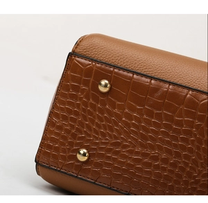 Macro detail of brown leather bag bottom with crocodile pattern and gold metal studs