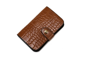 Detail of a brown crocodile pattern leather wallet with a round gold metallic buckle