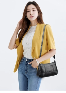 Détail d'un sac bandoulière en cuir noir grainé avec surpiqûres carrées et logo