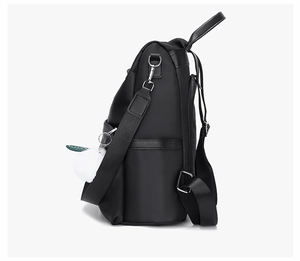 Vue latérale du sac à dos noir en tissu Oxford avec poche latérale et pompon blanc en peluche