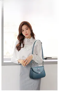 Blue leather crossbody bag with silver kangaroo logo shown on model in bright interior