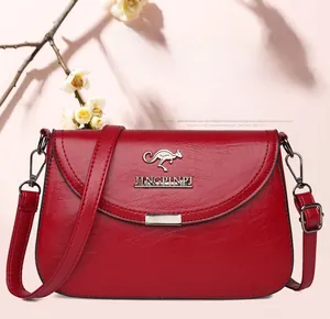 Detail of red leather crossbody bag with silver kangaroo logo and fine texture finish
