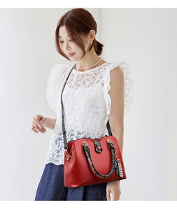Detail of red leather handbag featuring snakeskin print handles and a gold heart pendant