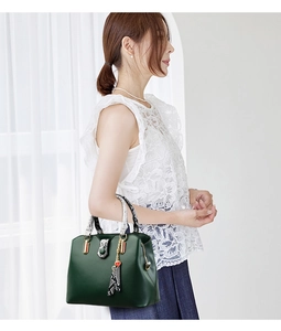 Detail view of dark green leather tote bag with snakeskin texture accents and heart charm