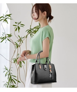 Detail of black faux leather handbag featuring snake-pattern handles and heart tassel charm