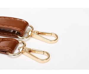 Detail of brown embossed leather straps with polished gold lobster clasps and stitching