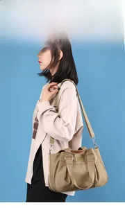 Khaki nylon shoulder bag with adjustable woven strap and reinforced handles on a blue background