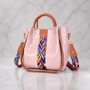 Detail view of pink croc-embossed bucket bag with colorful woven geometric strap