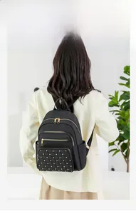 Detail view of black oxford backpack featuring quilted pocket and gold rivet accents