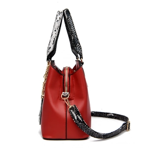 Large red tote bag with snake print handles and adjustable shoulder strap on white base