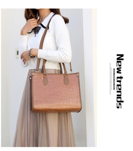 Detail of brown crocodile pattern tote bag with dual handles and long shoulder strap