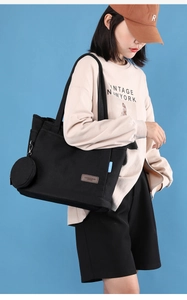 Detail of black canvas tote bag with small round coin purse and brown leather logo tag
