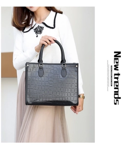 Chic black tote bag with crocodile pattern and golden studs held by a model