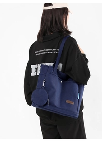 Blue canvas tote bag with front pocket detail and small hanging pouch on a model