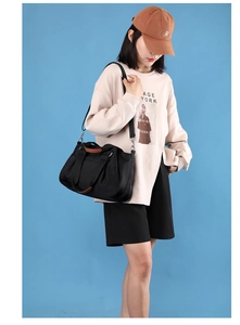 Nylon tote bag with brown leather accents shown as crossbody style on model with blue backdrop