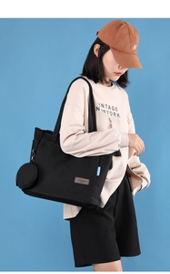 Detail of black canvas tote bag with brown leather logo patch and round coin purse