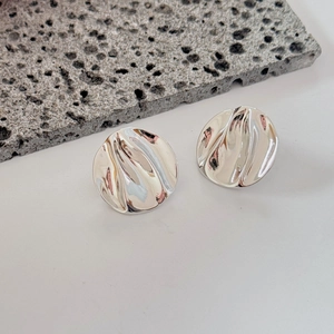 Irregular hammered silver round earrings displayed on stone over a white background
