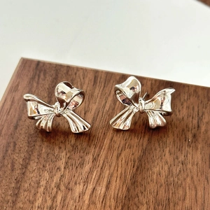 Elegant polished silver bow stud earrings displayed on dark walnut wood block