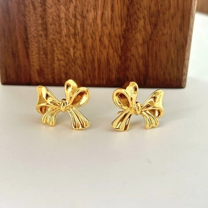 Polished gold bow stud earrings displayed on a rustic wood block with a minimalist aesthetic