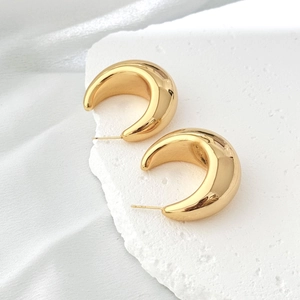 Minimalist gold-plated hollow crescent hoop earrings displayed on white stone texture