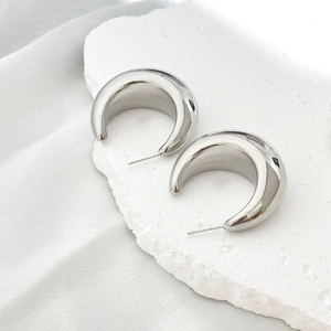 Modern silver chunky hoop earrings with a polished mirror finish on a stone surface
