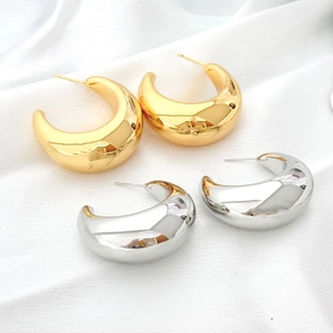 Polished chunky gold and silver C-shaped hoop earrings on elegant white satin fabric