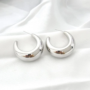 Detailed close-up of chunky silver C-shape hoop earrings on white silk fabric background