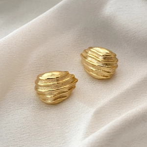 Detailed close-up of gold geometric textured stud earrings on soft beige silk background