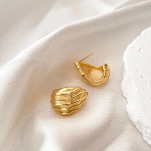 Golden irregular geometric ear studs with textured ripple design on white silk background