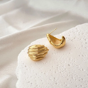 Macro detail of gold geometric shell earrings showing matte and polished textures