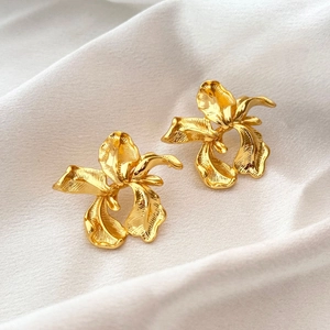 Macro shot of gold floral earrings with brushed metal texture on soft white silk fabric