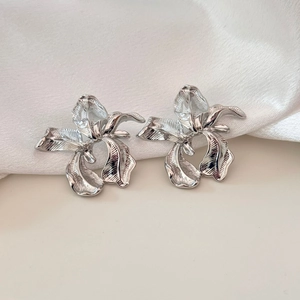 Macro shot of silver-toned iris flower earrings with metallic texture on white silk