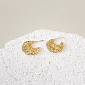 Detailed view of C-shaped gold earrings with hammered metal texture on white stone