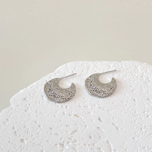 Macro view of minimalist C-shape silver earrings with textured hammered finish