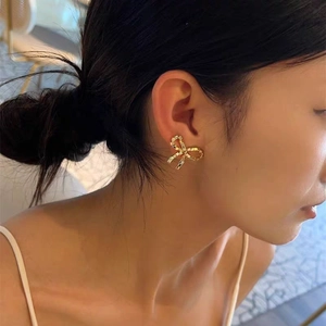 Elegant gold bow earrings with pavé square crystals shown on model's earlobe