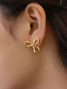 Macro close-up of a golden bow-knot stud earring with textured cubic metallic beads