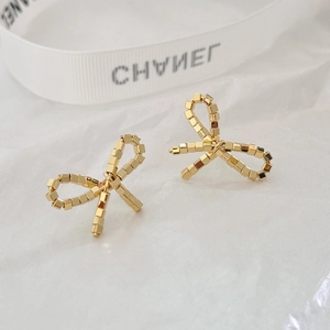 Macro shot of gold ribbon bow earrings crafted from linked metal cubes on white fabric