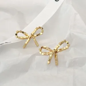 Macro shot of gold bow stud earrings with 3D beaded texture on a soft background