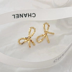 Detailed view of golden bow earrings featuring a textured cube design on white silk ribbon