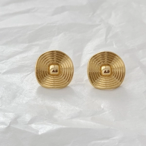 Detailed close-up of golden geometric stud earrings with textured concentric circle patterns