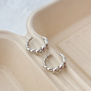 Macro detail of twisted silver C-shape stud earrings on a minimalist paper tray