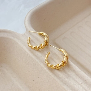 Detail of gold twisted rope texture earrings with a minimalist C-shape design and glossy finish