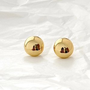 Macro detail of polished gold ball stud earrings on a textured white background