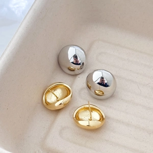 Macro detail of minimalist round silver ball studs and golden dome earrings on a tray