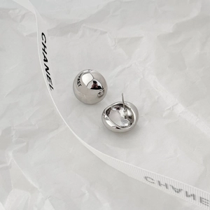 Macro shot of minimalist polished silver ball stud earrings on textured white paper