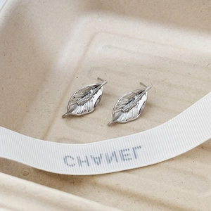 Minimalist silver leaf stud earrings with high polish finish on a textured beige tray