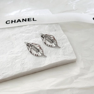Detailed close-up of silver leaf earrings with intricate veins on white textured stone