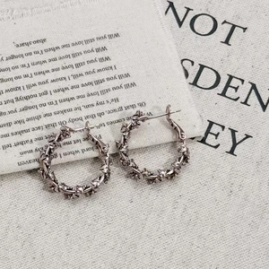 Detailed view of silver twisted rope hoop earrings on vintage fabric background