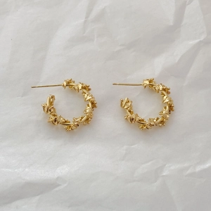 Detailed view of gold C-shaped earrings with irregular crushed lava texture on white paper
