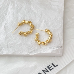 Detailed close-up of golden C-shape earrings with textured vine pattern on stone pedestal